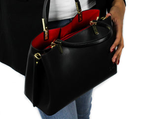 A model holding open a leather handbag that is black on the exterior and red on the interior - a slate LYNETTE handbag from Pamo